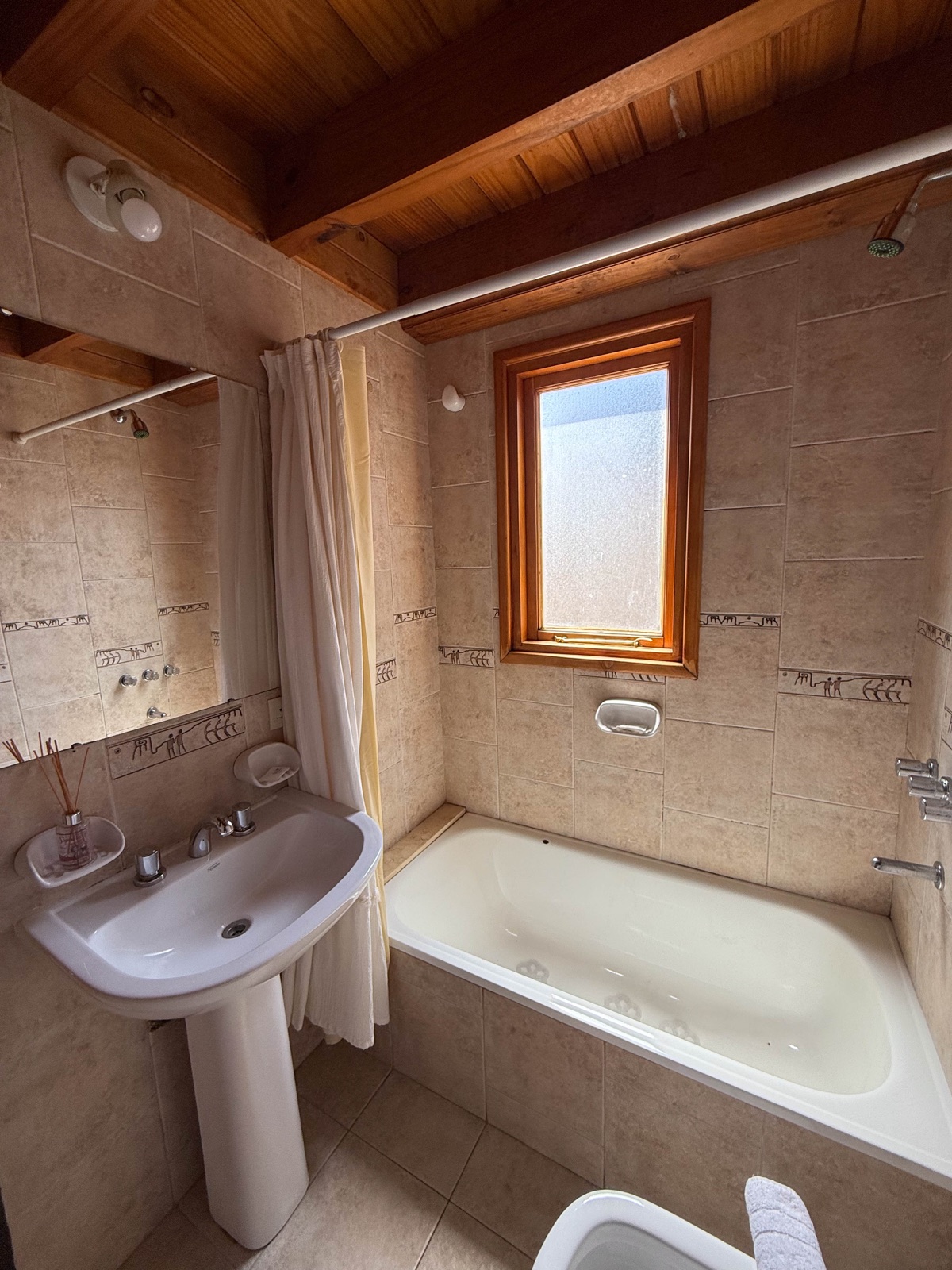 Baño con bañera, lavabo con pedestal y techo de madera